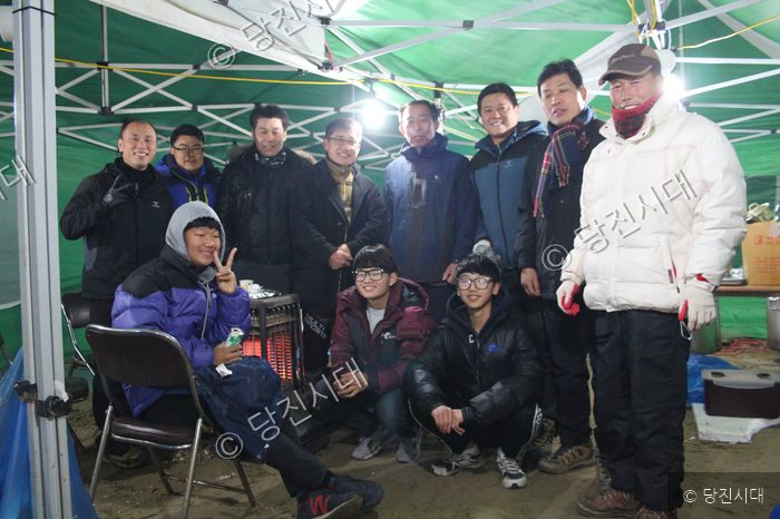 텐트 안에서 모인 주민들이 환하게 웃으며 기념사진을 찍고 있다.