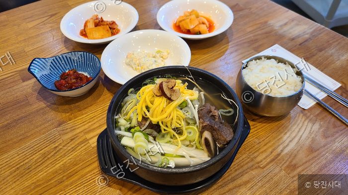 식당 테이블 위에 갈비탕과 다양한 밑반찬이 차려져 있다.