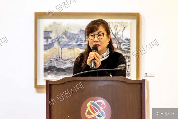한 여성이 연단에서 마이크를 잡고 발표를 하고 있다.