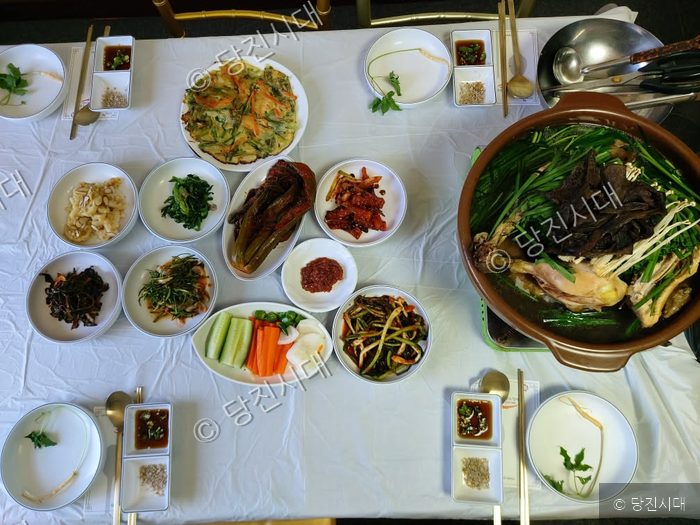 식탁 위에 능이닭백숙과 다양한 밑반찬이 차려져 있다.