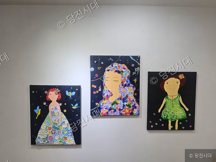 갤러리 벽면에 다양한 인물이 그려진 회화 작품 세 점이 걸려 있다.