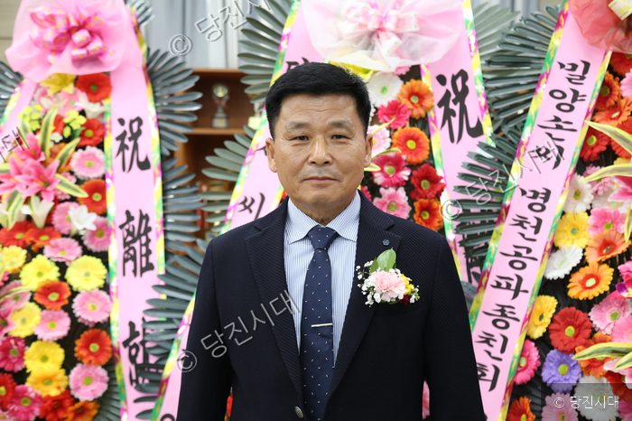 한 남성이 정장 차림으로 행사장 화환 앞에서 포즈를 취하고 있다.
