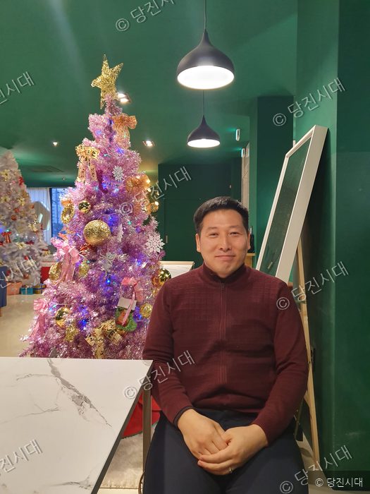 한 남성이 실내에서 카메라를 향해 미소 짓고 있다.