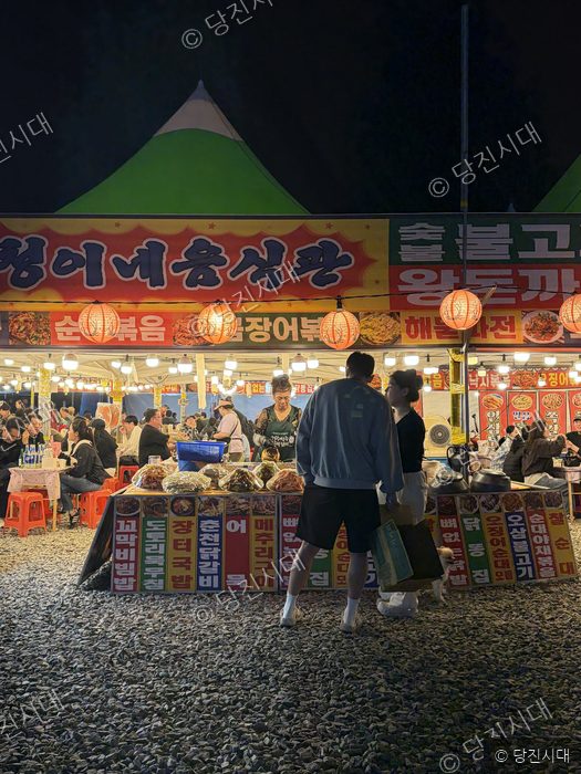 밤거리의 축제 부스에서 사람들이 음식을 고르고 있다.