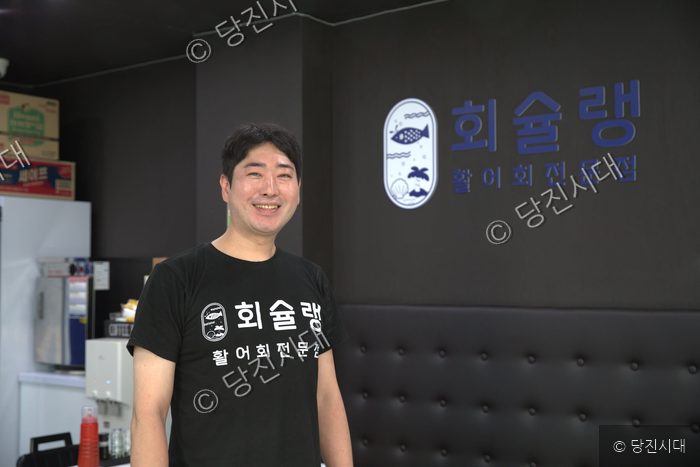 식당 대표가 가게 내부에서 환하게 미소 짓고 있다.
