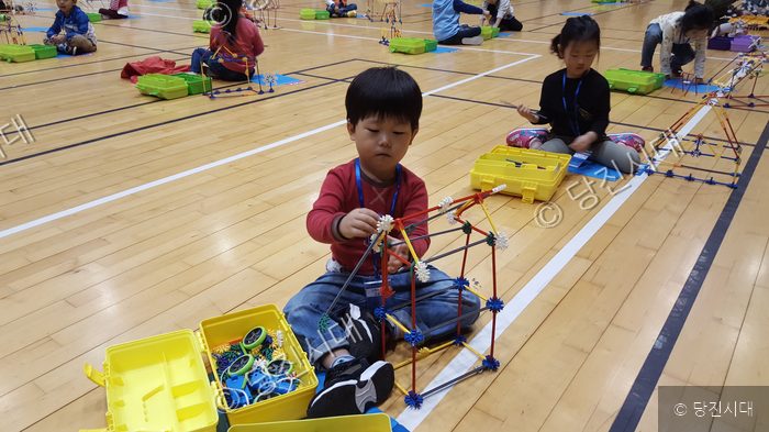 어린이들이 체육관 바닥에 모여 교구로 창의적인 구조물을 만들고 있다.