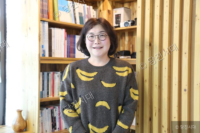 이가연 씨가 책장이 있는 실내에서 미소 지으며 서 있다.