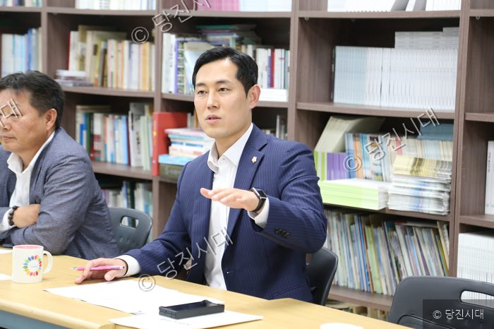 회의 테이블에 앉아 손짓하며 발언하는 남성의 모습.