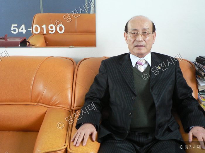 한 남성이 소파에 앉아 정면을 바라보고 있다.