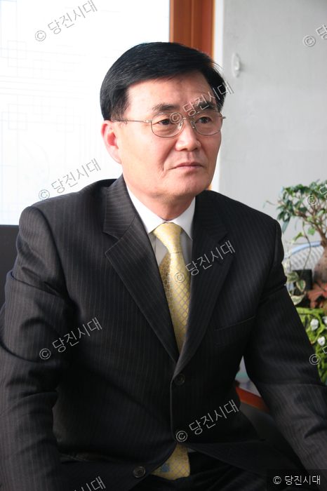 정장 차림의 남성이 의자에 앉아 정면을 응시하고 있다.