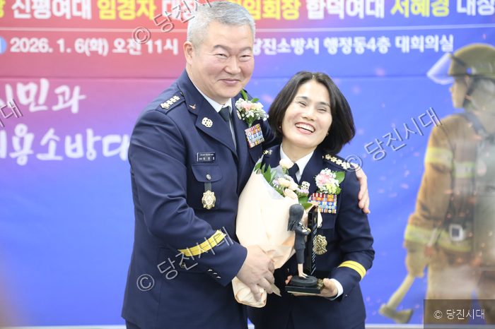 소방관들이 대회의실에서 기념패와 꽃다발을 들고 미소 짓고 있다.