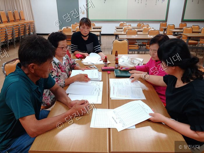 주민들이 교육장 테이블에 모여 새마을 관련 서류를 검토하고 있다.