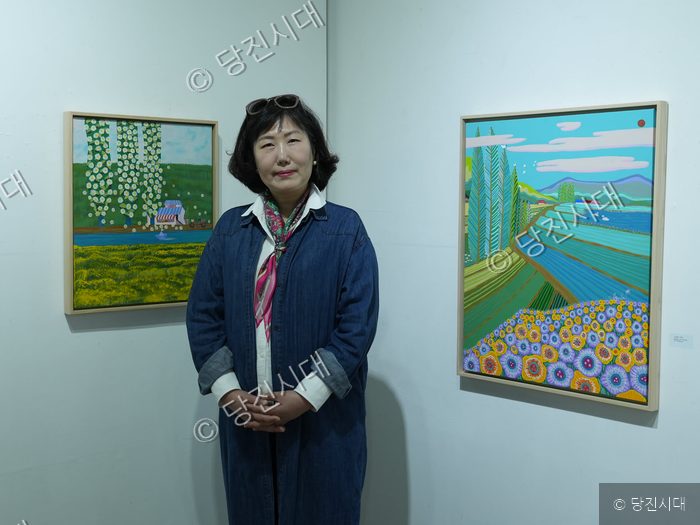 한 화가가 자신의 미술 작품들 사이에 서서 포즈를 취하고 있다.