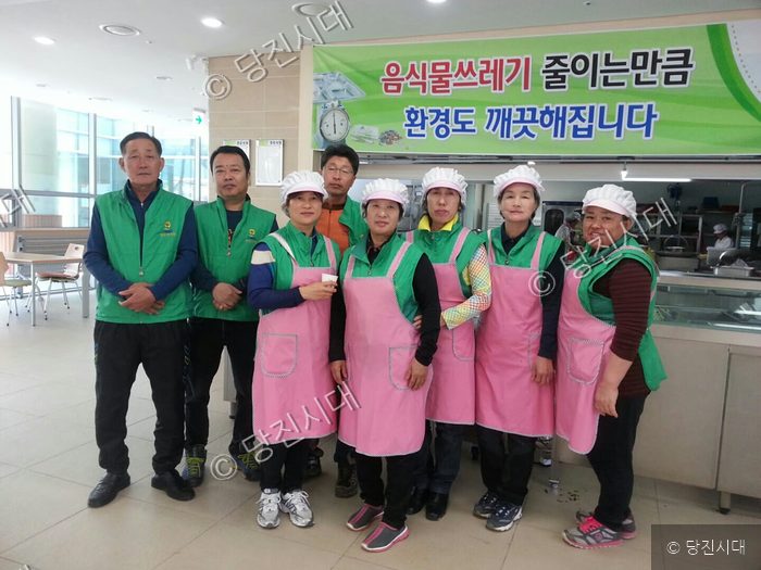 봉사자들이 식당에서 음식물쓰레기 줄이기 캠페인 현수막 아래에 모여 있다.