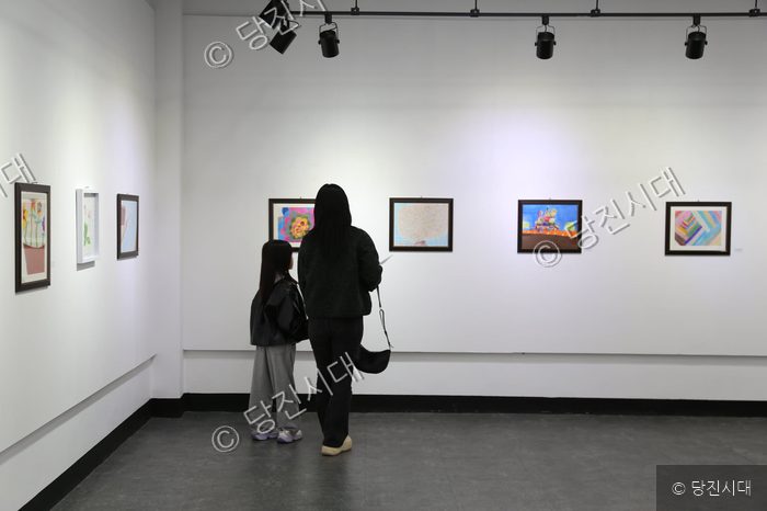 한 모녀가 미술관에서 어린이들의 그림 작품을 감상하고 있다.