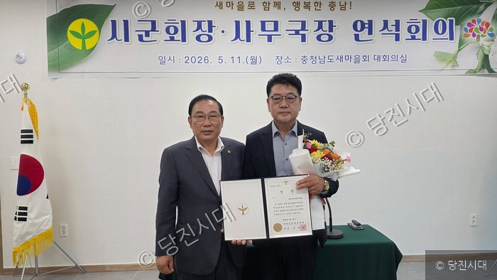 충청남도새마을회 회의실에서 두 남성이 상장과 꽃다발을 들고 기념 촬영을 하고 있다.