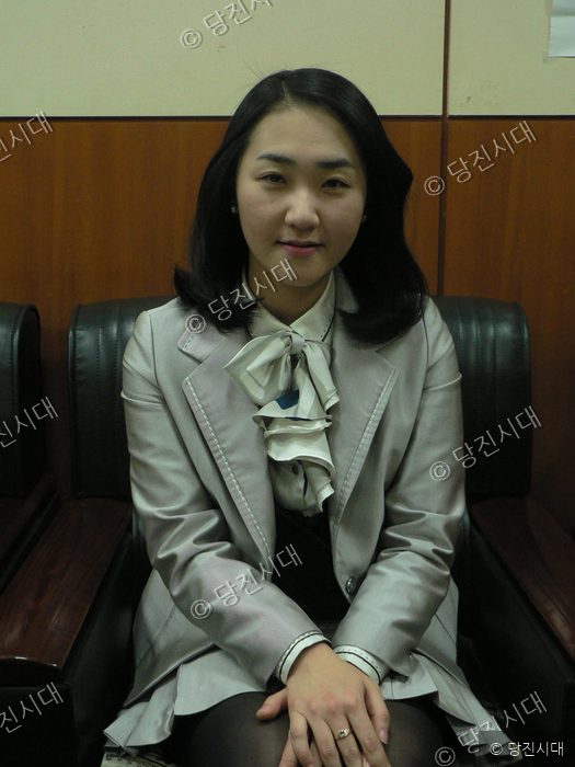 한 여성이 의자에 앉아 카메라를 바라보고 있다.