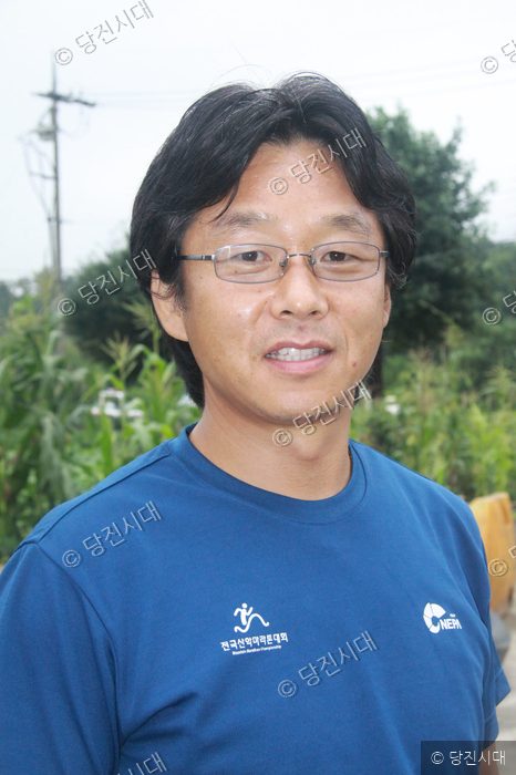 김장환 대표가 푸른색 티셔츠를 입고 카메라를 향해 미소 짓고 있다.