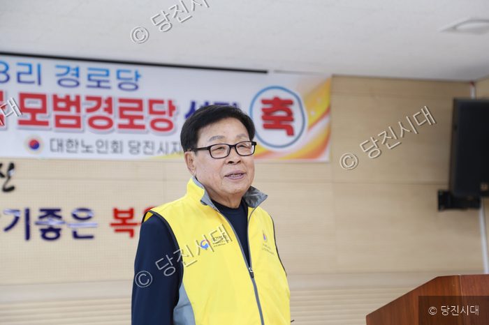노란색 조끼를 입은 남성이 복운3리 경로당 행사에서 발언하고 있다.