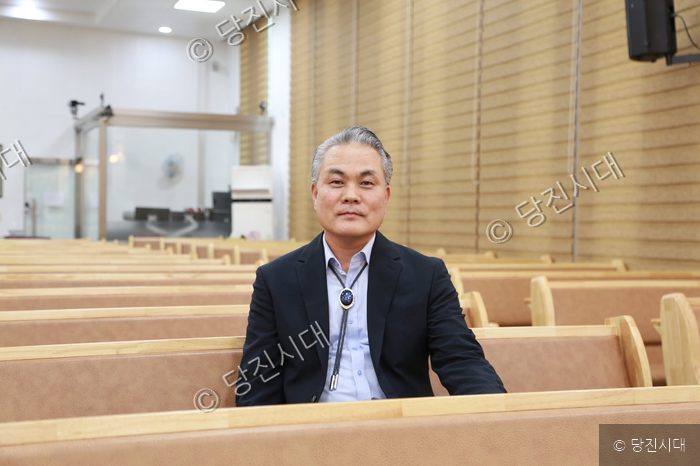 홍용관 감리사가 예배당 의자에 앉아 카메라를 응시하고 있다.