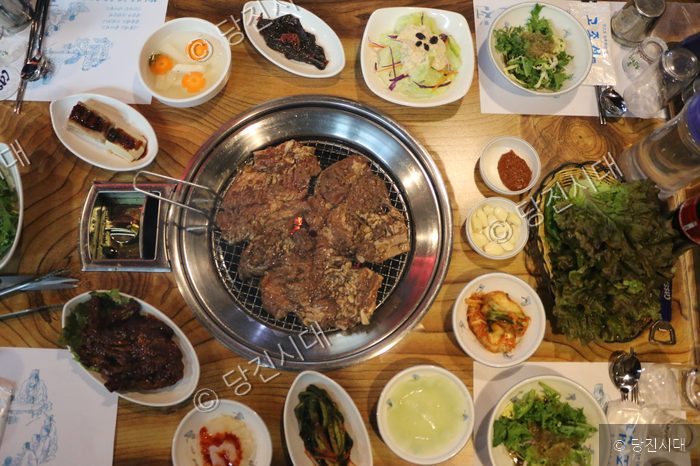 식당 테이블 위에 갈비와 다양한 반찬들이 푸짐하게 차려져 있다.