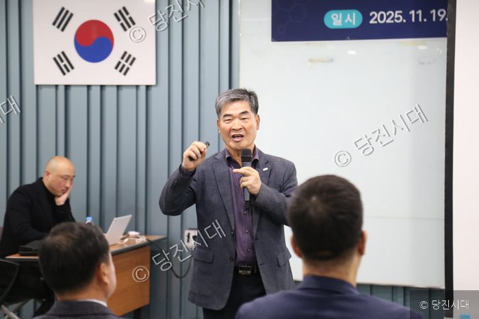 한 남성이 강의실에서 마이크를 들고 발표하고 있다.