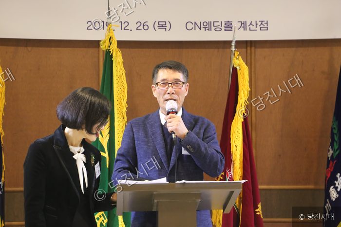 이재욱 회장이 마이크를 잡고 발언하고 있고, 옆에는 여성이 서 있다.