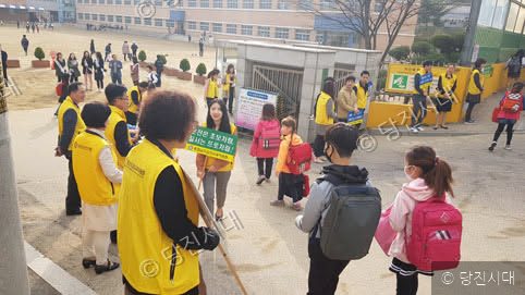 노란 조끼를 입은 자원봉사자들이 학교 앞에서 교통안전 캠페인을 벌이고 있다.