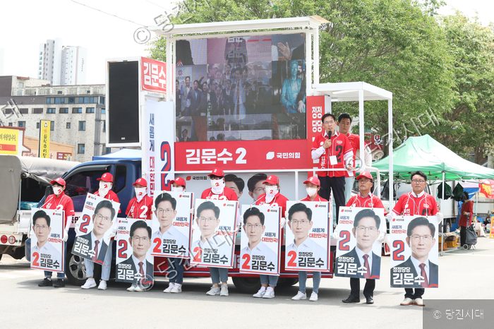국민의힘 선거 유세 차량 앞에서 지지자들이 후보 포스터를 들고 서 있다.