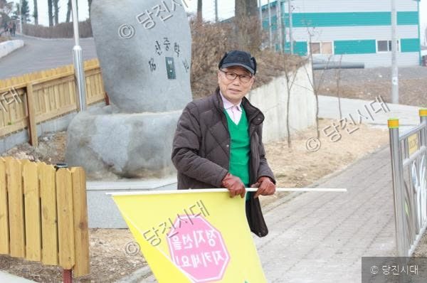 노인이 학교 근처에서 노란색 깃발을 들고 서 있다.