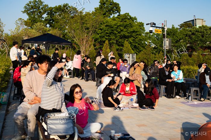 사람들이 야외 광장에 모여 앉아 영화를 관람하고 있다.