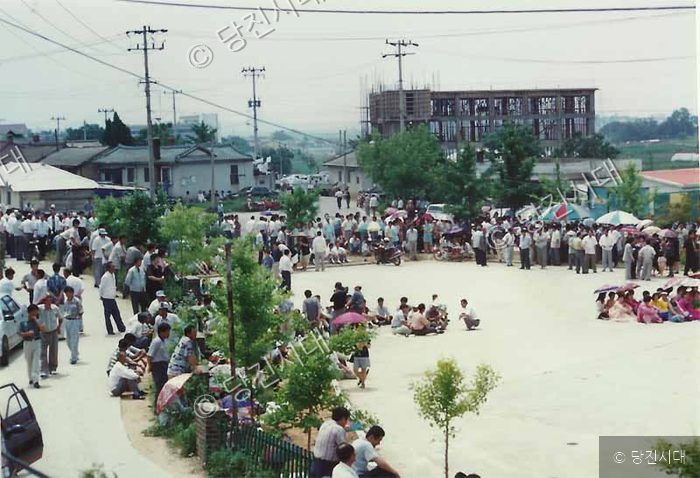 많은 사람들이 야외 광장에 모여 행사를 지켜보고 있다.