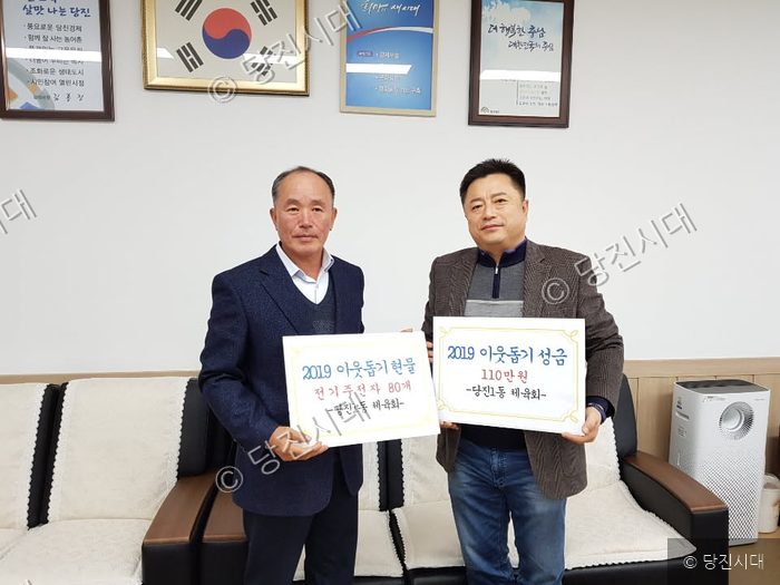두 남자가 이웃돕기 성금과 현물 피켓을 들고 기념촬영을 하고 있다.