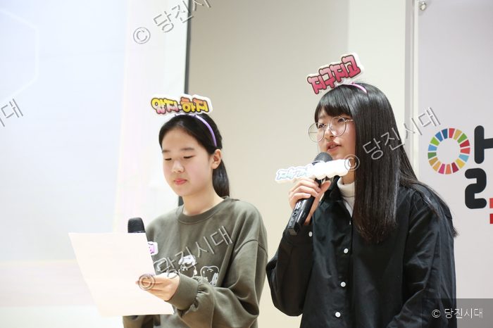 두 청소년이 무대에서 마이크를 들고 발표를 하고 있다.