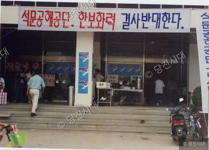 사람들이 건너편 건물 앞에서 한보화력 반대 시위를 벌이고 있다.