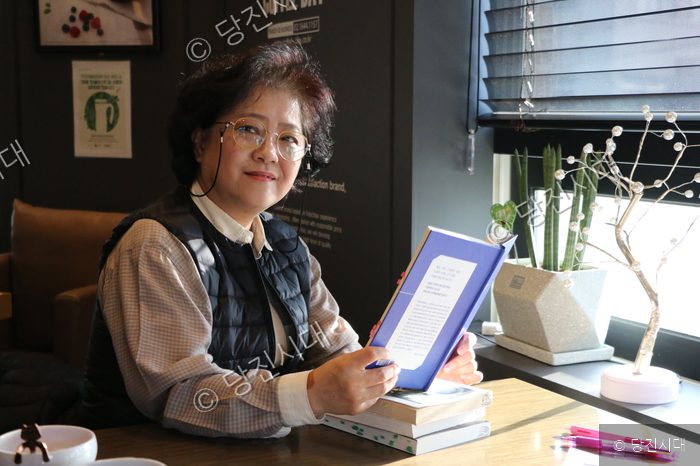 임소희 회원이 카페 창가에서 책을 펼쳐 보이고 있다.