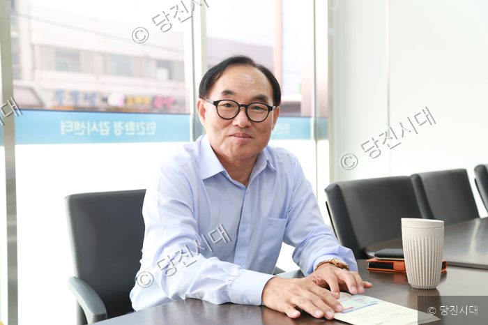 한 남성이 사무실 책상에 앉아 카메라를 바라보고 있다.