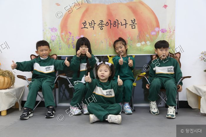 초록색 체육복을 입은 어린이들이 나란히 앉아 포즈를 취하고 있다.