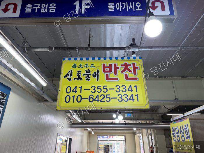 실내 시장에 반찬 가게 안내 표지판이 걸려 있다.