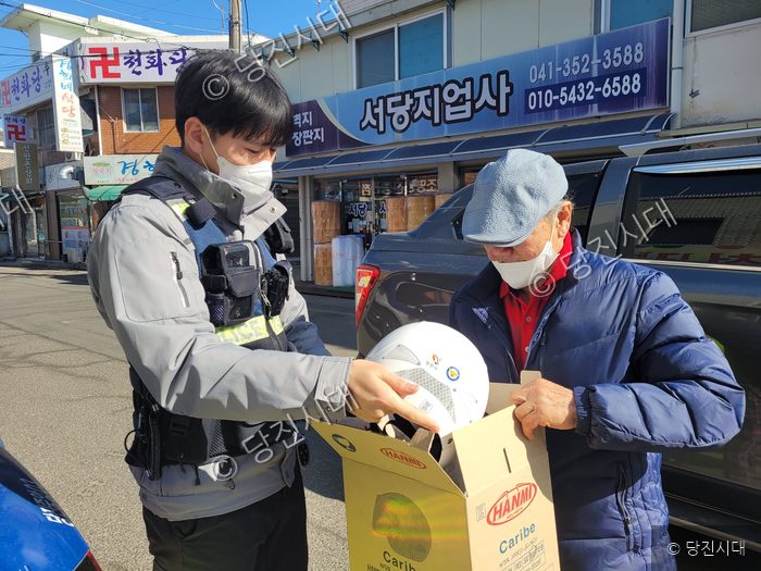 경찰관이 어르신에게 안전모를 전달하고 있다.