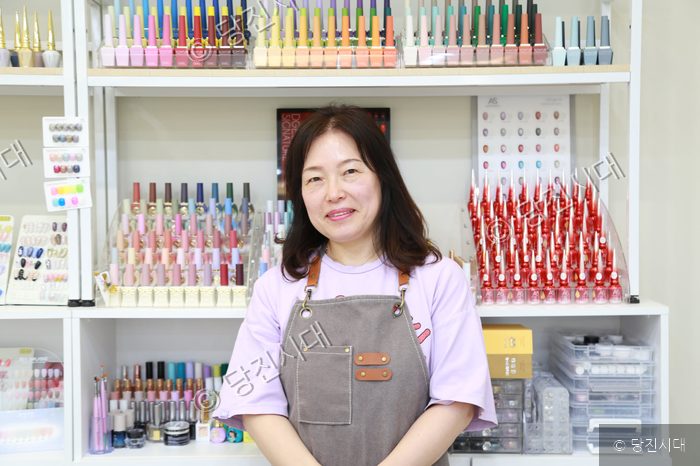 네일숍 대표가 매장 내부에서 환하게 미소 짓고 있다.