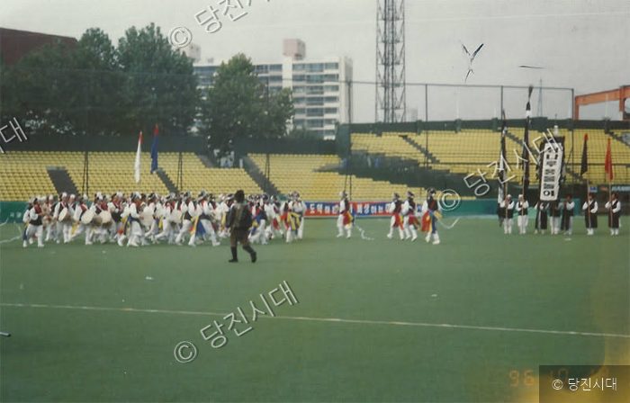 운동장에서 사람들이 전통악기를 연주하며 행진하고 있다.
