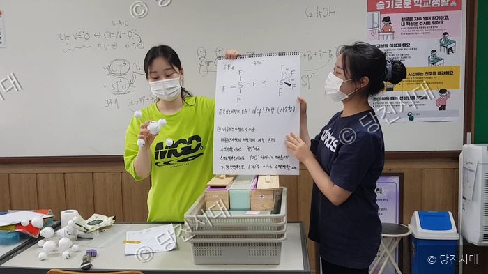 두 학생이 교실에서 화학 구조 모형과 학습 발표 자료를 들고 있다.