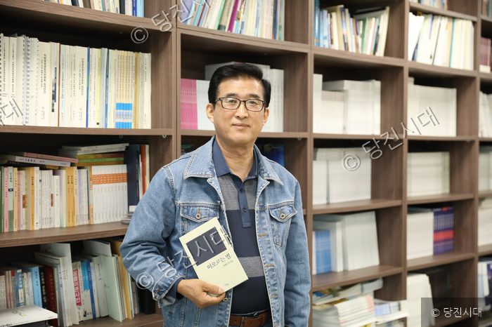 이재성 씨가 책을 들고 서서 카메라를 응시하고 있다.
