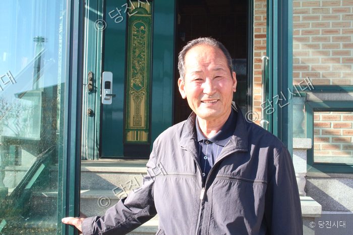 우강면의 한 주민이 집 앞에서 미소를 지으며 서 있다.