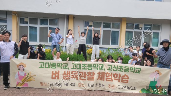 학생들과 주민들이 벼 생육 관찰 체험학습 현수막을 들고 기념 촬영을 하고 있다.