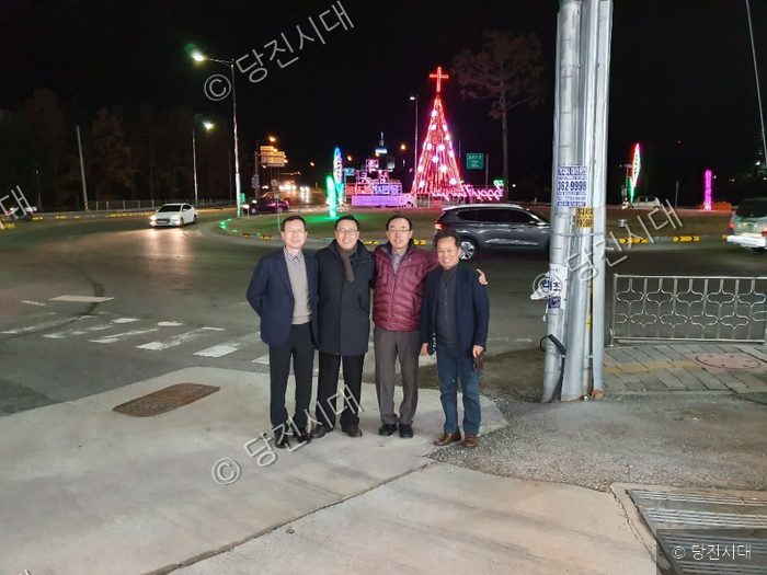 네 명의 남성이 성탄트리 점등 행사장에서 기념 촬영을 하고 있다.