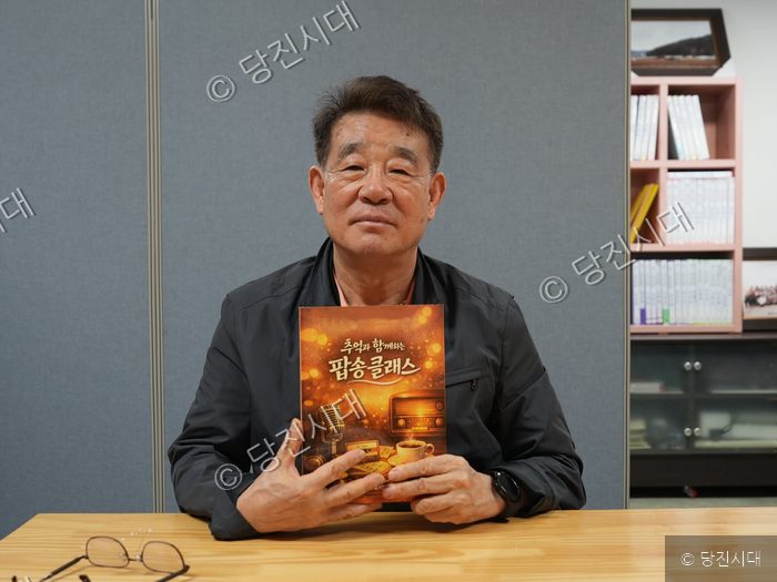 남성이 책을 들고 카메라를 바라보고 있다.