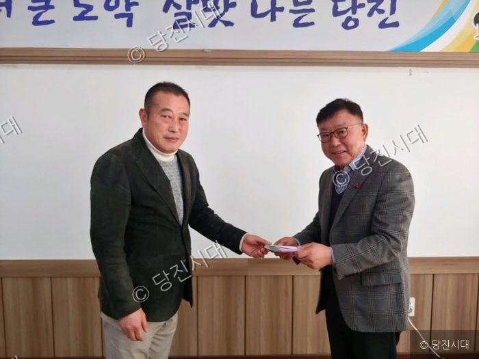 한 남성이 다른 남성에게 장학금을 전달하고 있다.
