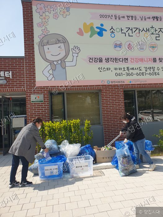 두 사람이 건물 앞에서 재활용품을 분류하고 있다.